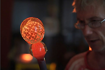 Mark Armstrong inspecting a glowing buble of molten glass